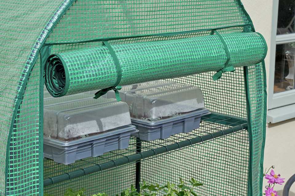 A close up of a green house with pots in it.