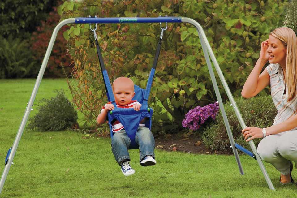 A baby swinging in the Chad Valley Kids' active 2-in-1 swing with mum supervising.