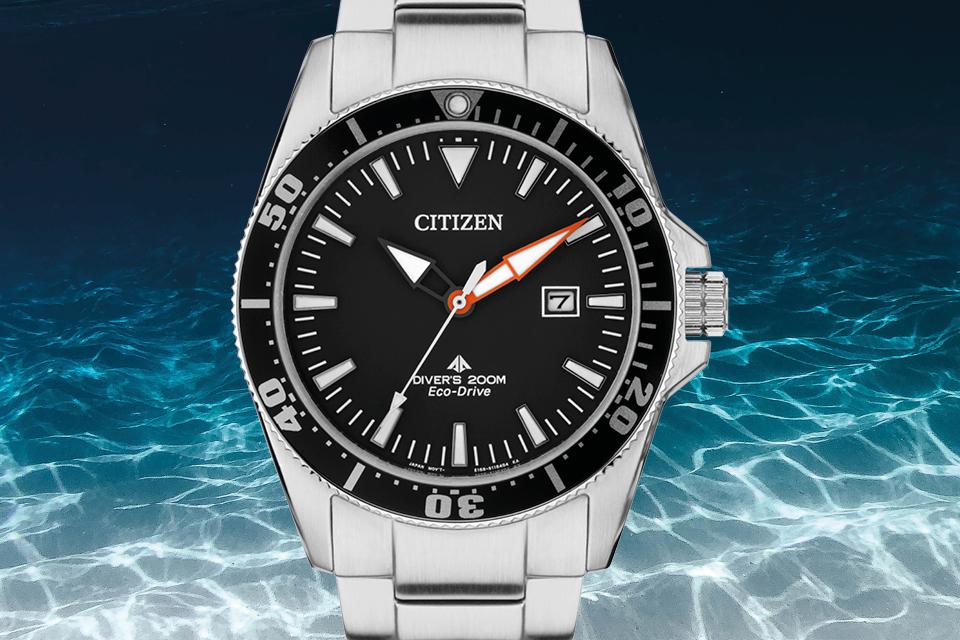 Image shows a Stainless steel Divers watch with a black dial. In the background is the ocean floor. 