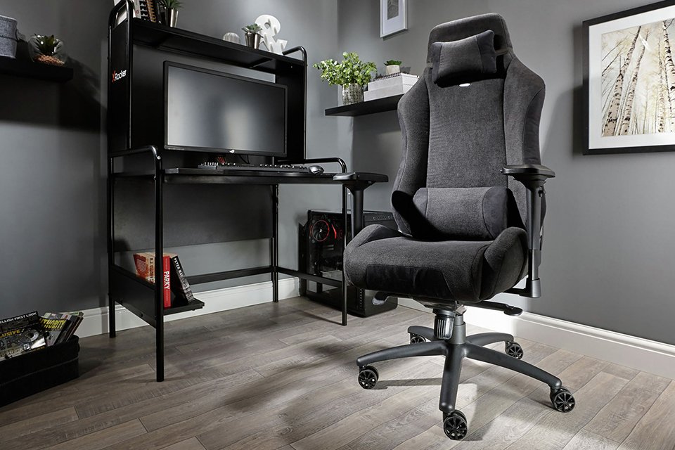 A gaming set up with a black table, a screen and an X Rocker Messina fabric black gaming chair.