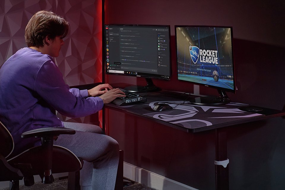 A boy celebrating over a win near a gaming set up while sitting across an X Rocker Cougar XL gaming desk.