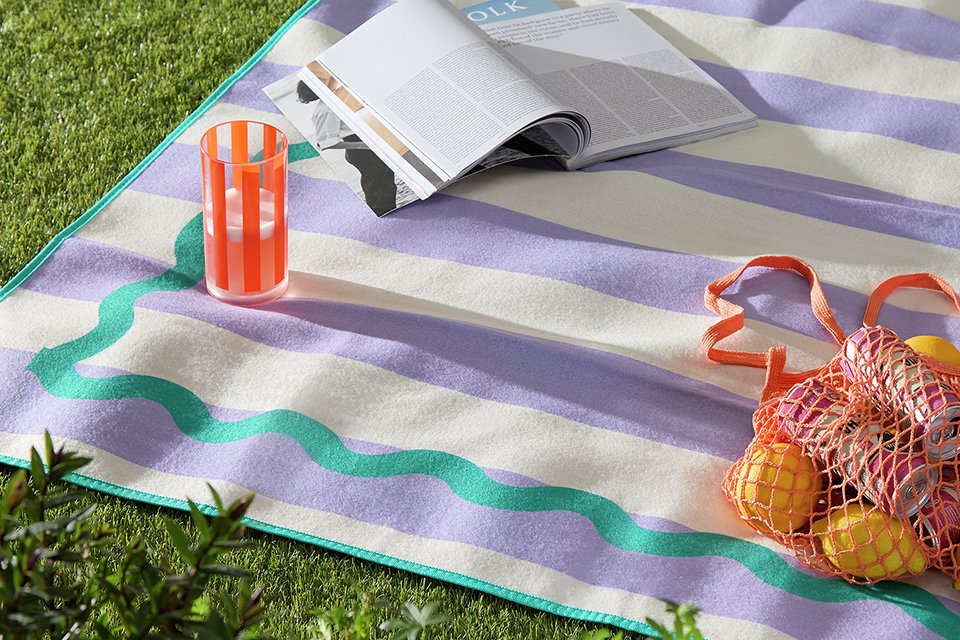 A Home Scandi Wiggle Picnic Rug with a book, a beverage and a bag of food on it.