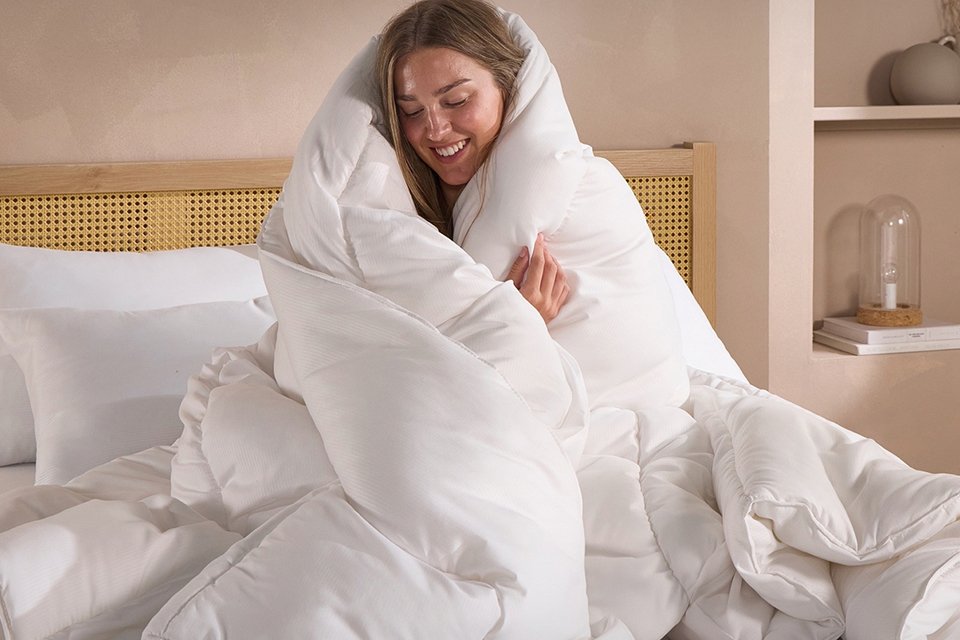 A woman sitting with a Snuggledown Scandi Classic 13.5 tog duvet wrapped around her.