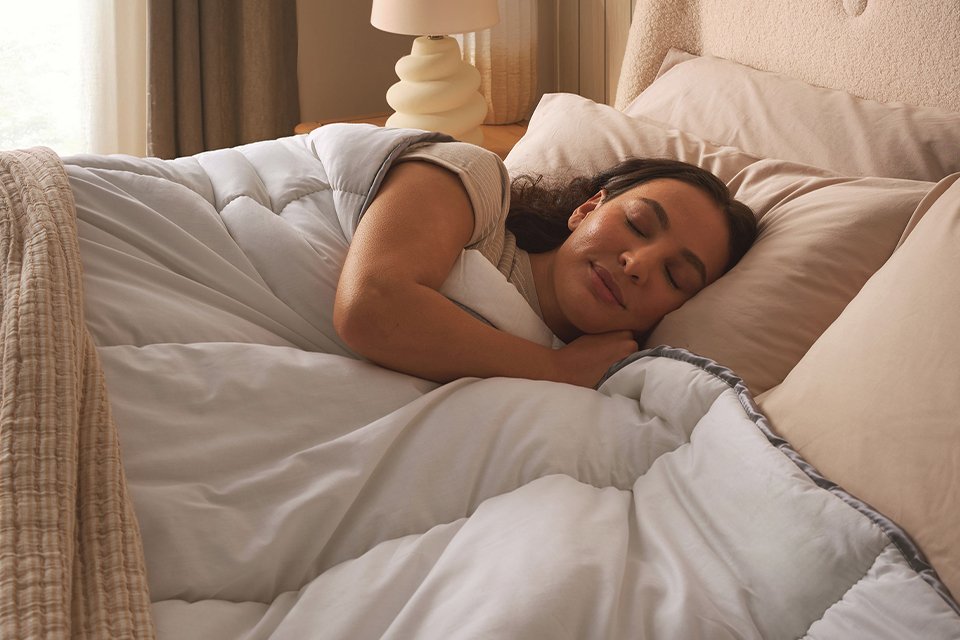 A woman sleeping under a Sleepeezee Sumptuous Cotton 10.5 tog duvet.