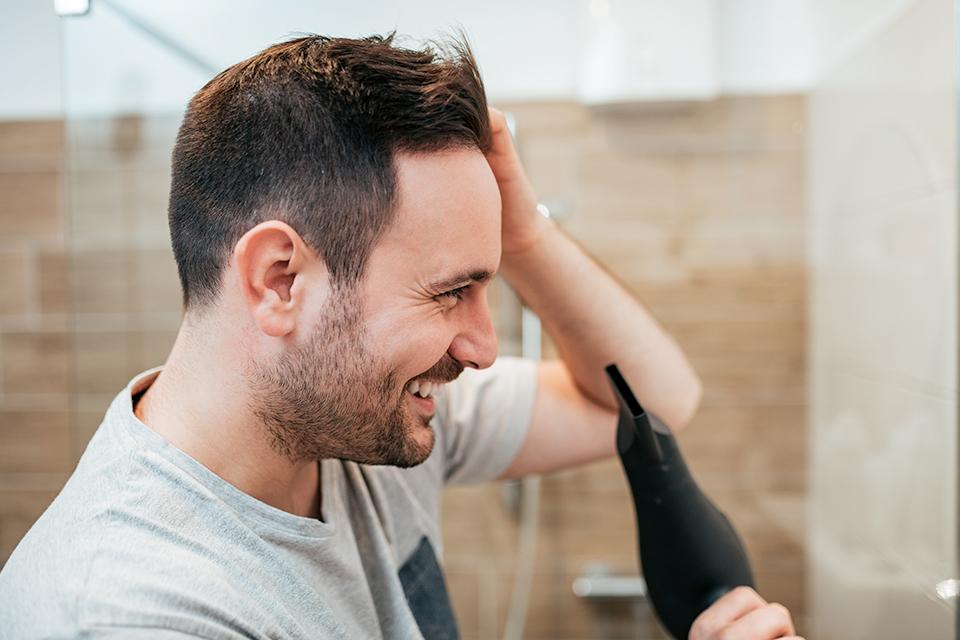 A man happily styling his hair in front of a mirror.