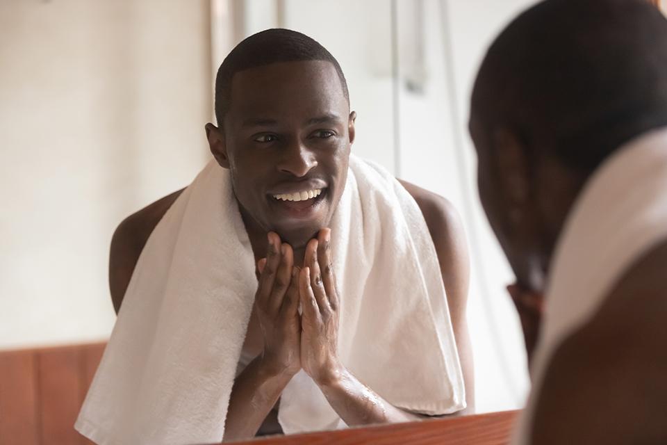 A man smiling looking at the mirror having just shaved with a towel around his neck.