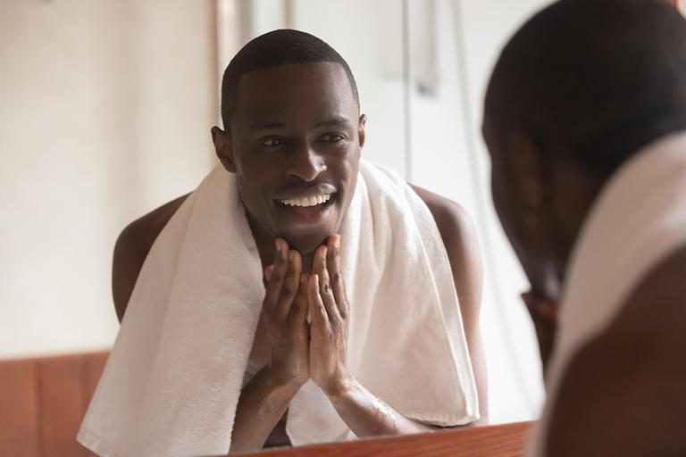Man with a towel around his neck, looking at his reflection in a mirror.