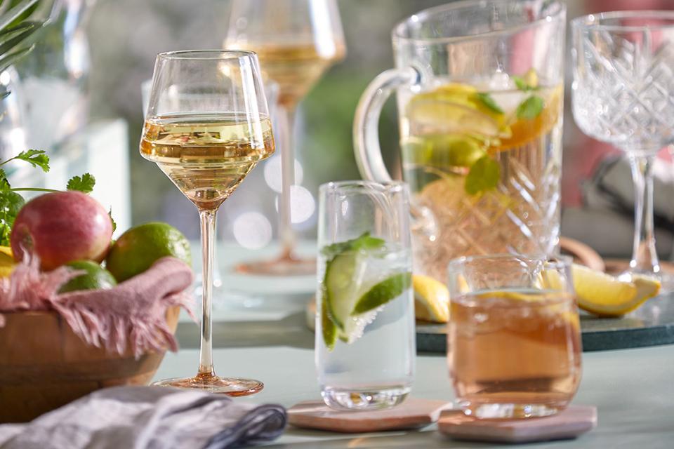 Close up of glass tumblers and wine glasses on a dining table.