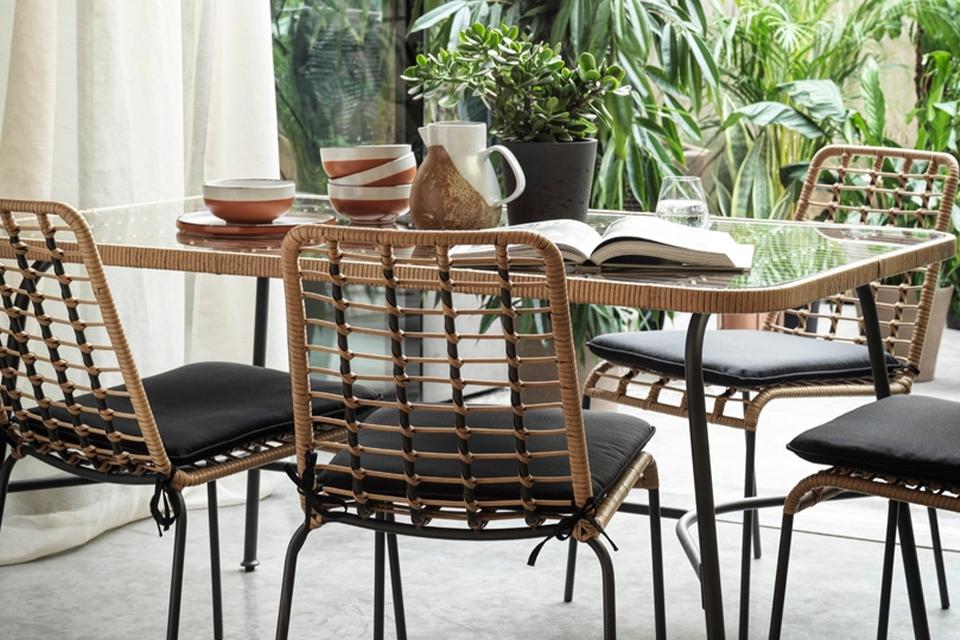 A glass and metal bistro set on a patio with tableware, a potted plant and a book on it.