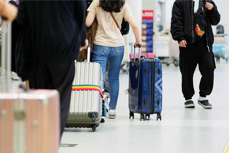 A picutre with people walking on an airport with 8 and 4 wheel suitcase. 
