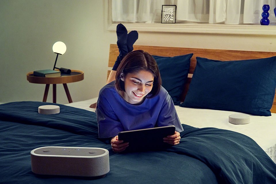 : A girl laying down with a tablet in hand and HTAX7 home theatre speaker next to her.