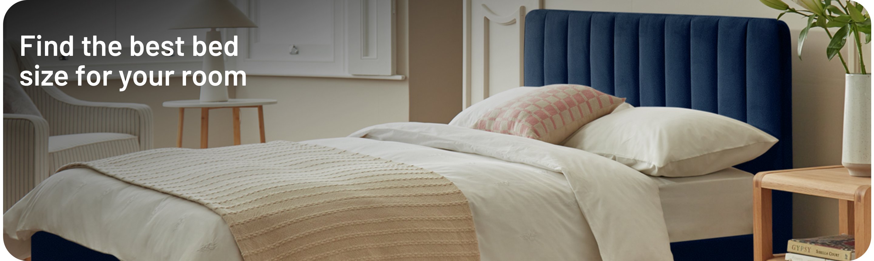 Throw, pillows and blanket neatly layered over a dark ink blue ottoman bed in a bedroom.