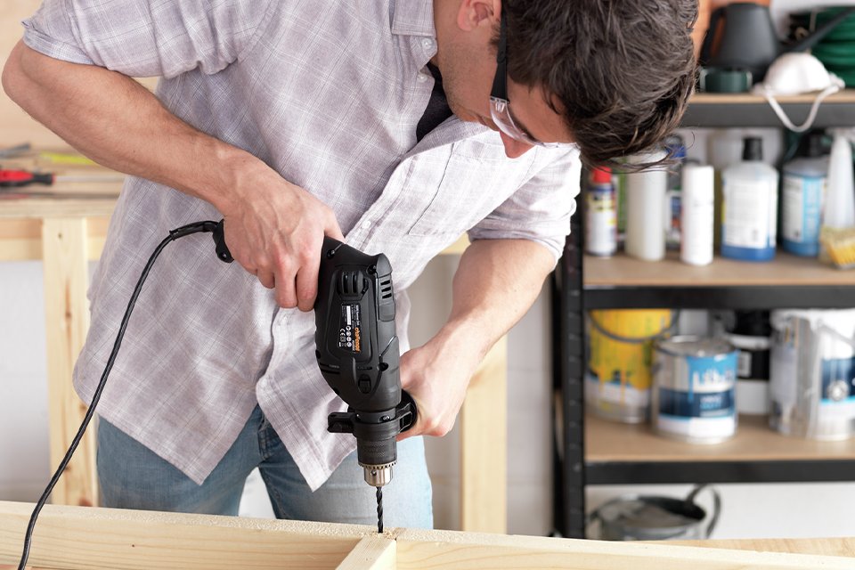 A man using a 500W Challenge corded impact drill to drill into a piece of wood.
