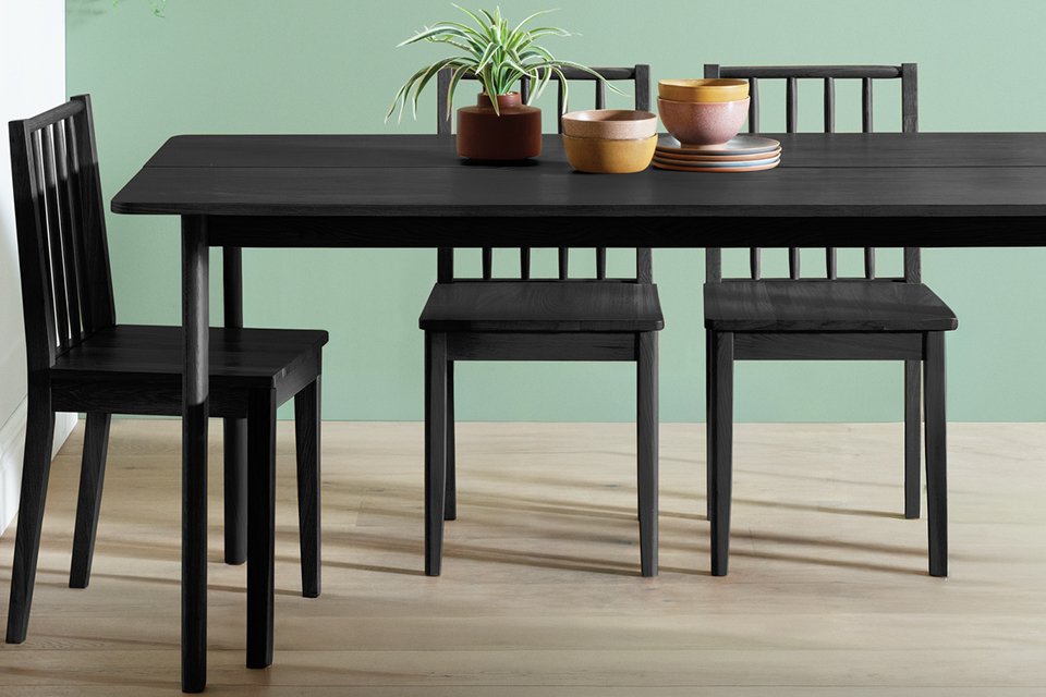 A Habitat Nel wood veneer black 4 seater dining table in a dining room with matching chairs placed around it. 