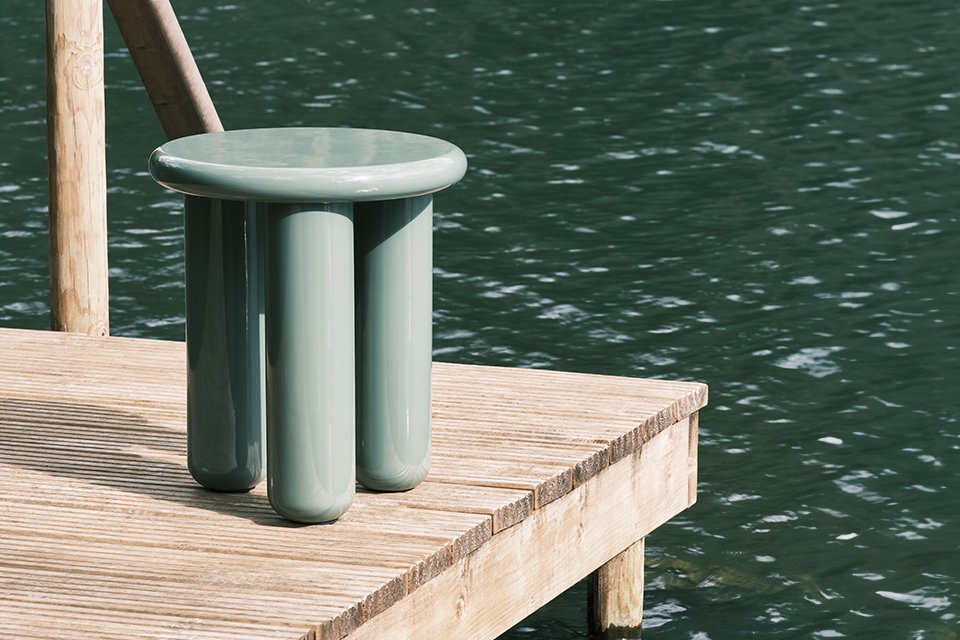 A Habitat side table in green colour placed on a lakeside deck. 