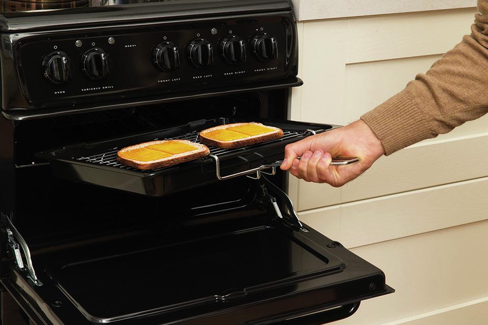 A man cooking cheese on toast, on an oven grill.