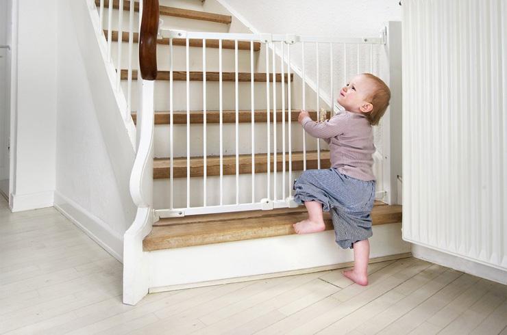 A baby trying to open the safety gate at the start of a staircase.