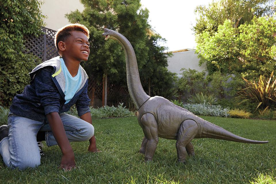 Boy playing with a Jurassic World Super Colossal Brachiosaurus outside in the garden.