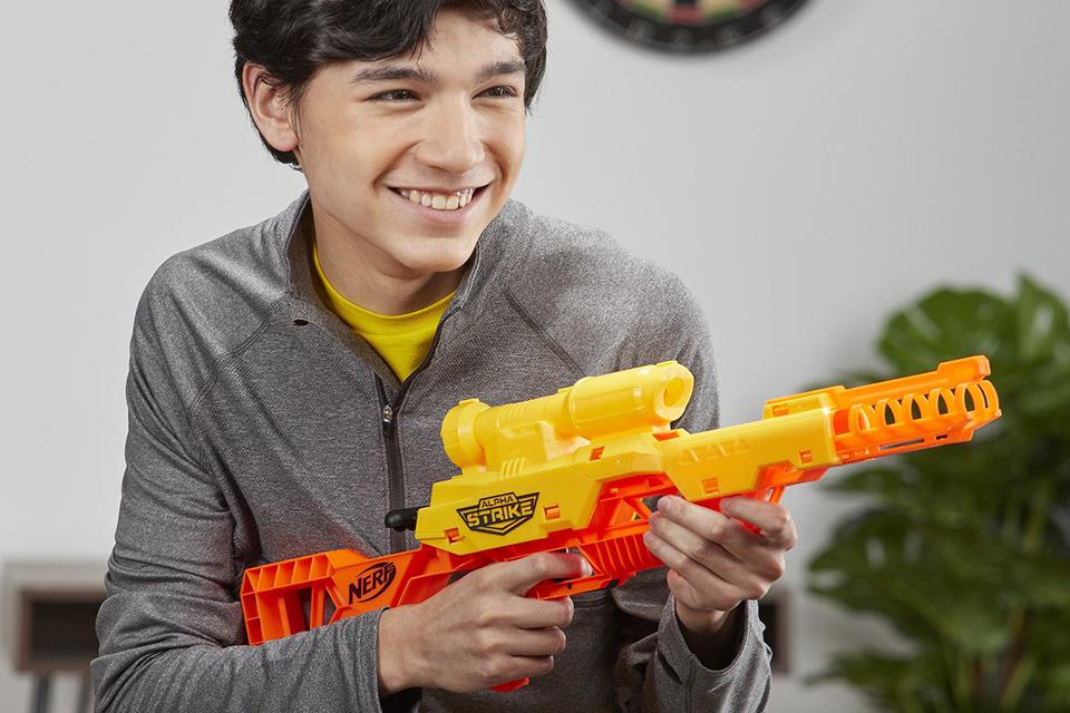 A boy in a living room, holding a Nerf Alpha Strike blaster.