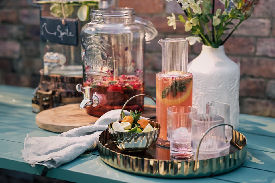 Cocktail at dusk on a gold tray with cocktail mixer.