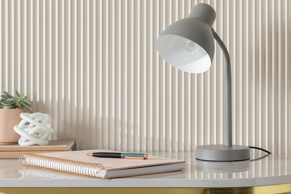 Argos Home desk lamp in flint grey colour placed on a white and gold table next to a notebook.