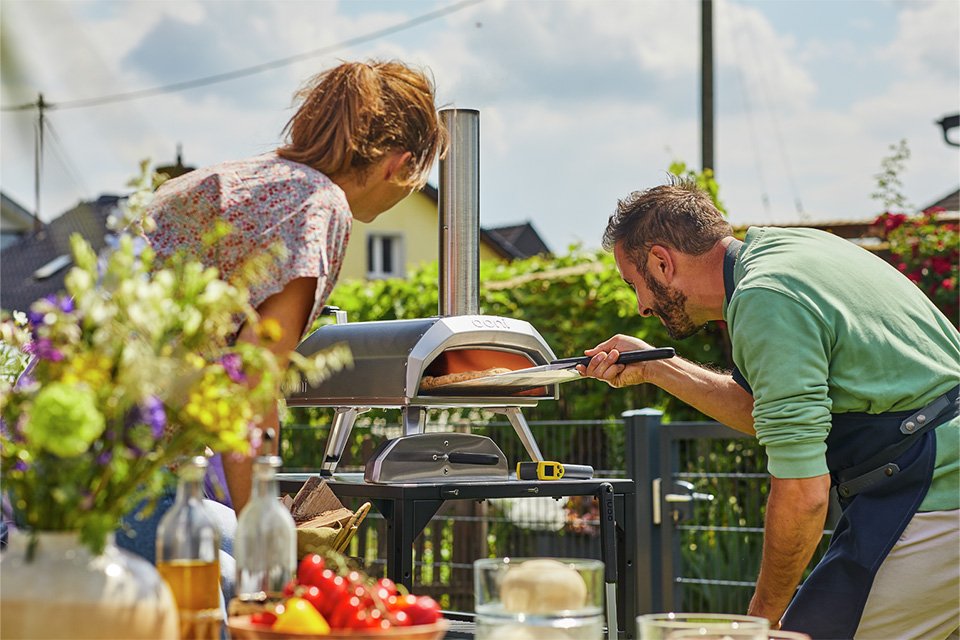 A man putting a pizza into Ooni Karu 12 Multi-fuel Pizza Oven to bake.