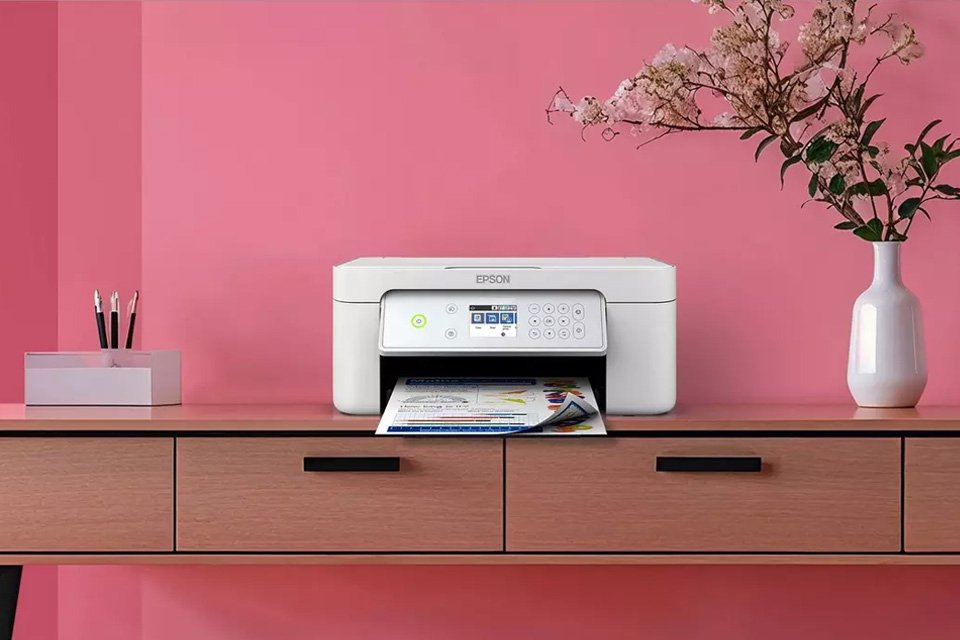 A white Epson printer placed on a table against a pink wall.