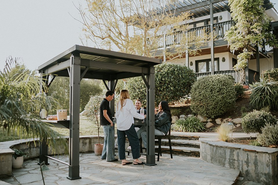 A group of friends hanging out at a Keter Signature Garden Grill Gazebo.