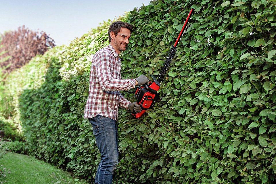 A man using an 18V Einhell cordless hedge trimmer to cut hedges.