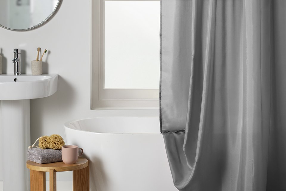 A grey shower curtain hanging on a rail above the bathtub.