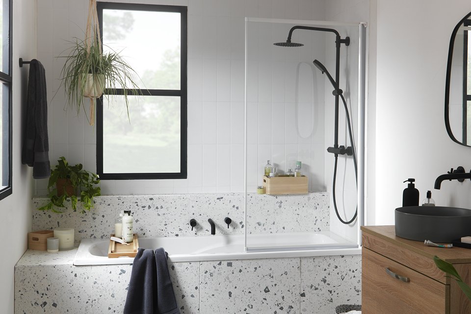 A white bathroom with a 3mm Fully Framed Bath Screen, wooden under-sink storage and black fittings.