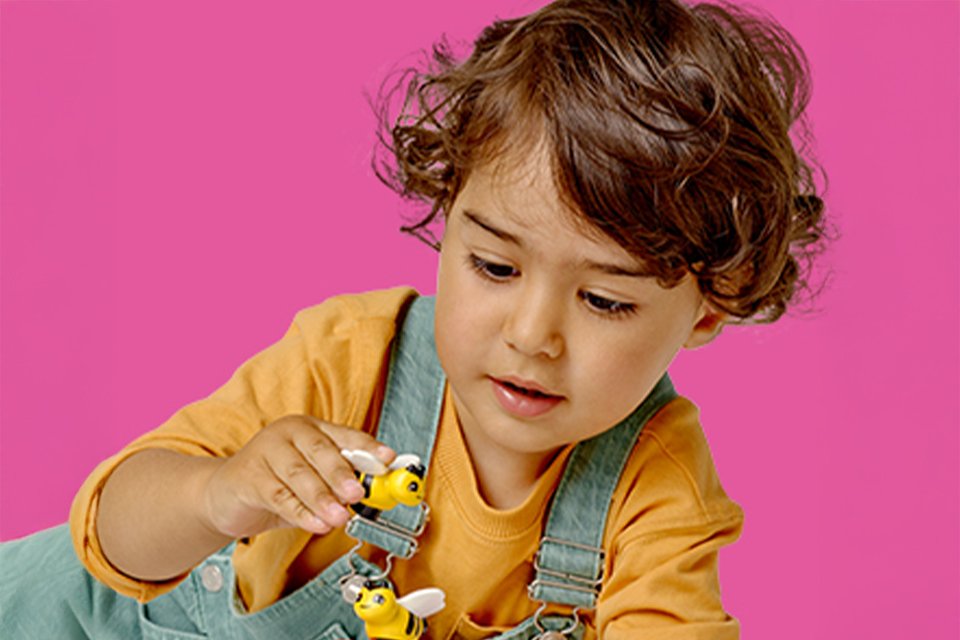 Little girl on a pink background playing with LEGO® bees.