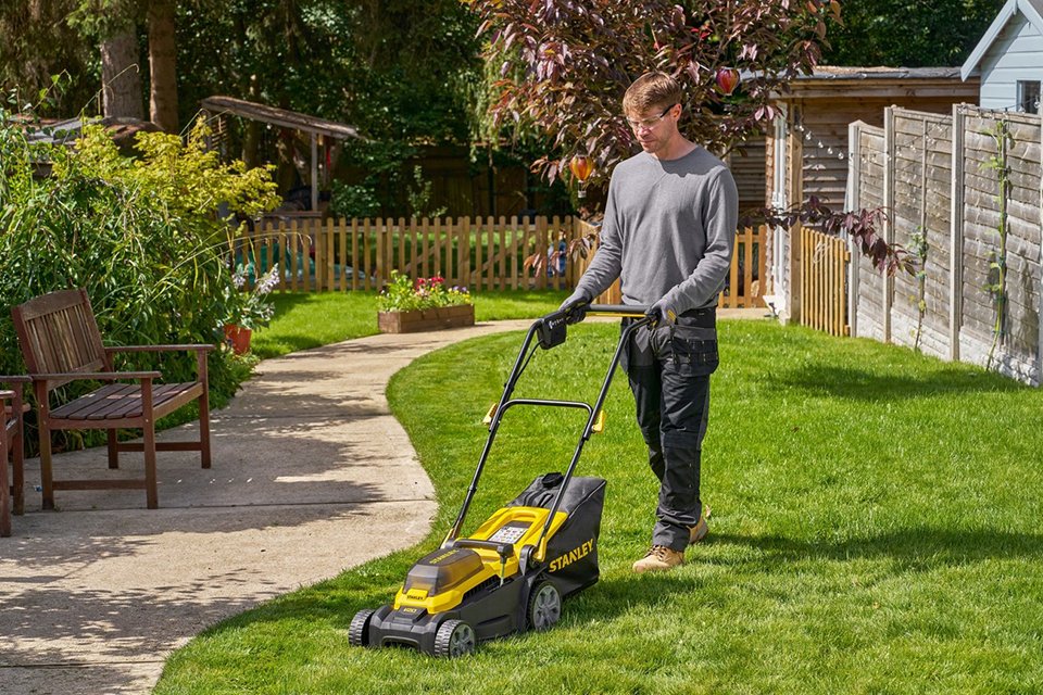 A man using an 18W STANLEY V20 cordless rotary lawnmower to mow his lawn.