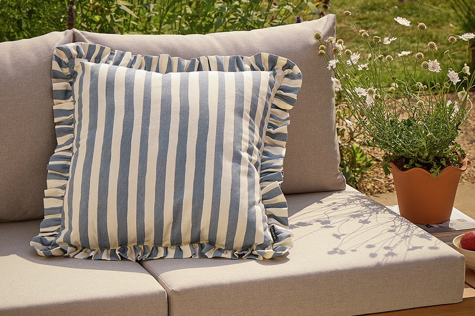 An Argos Home Blue striped outdoor cushion with a frill placed on a garden sofa set.