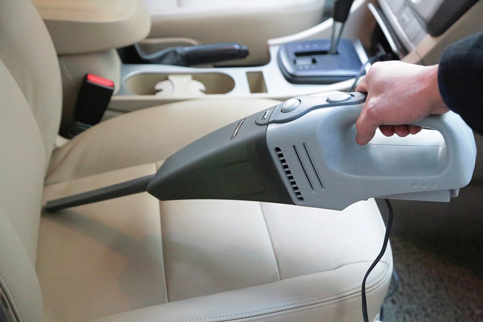 A person claening their car using a hand-held vacuum cleaner.