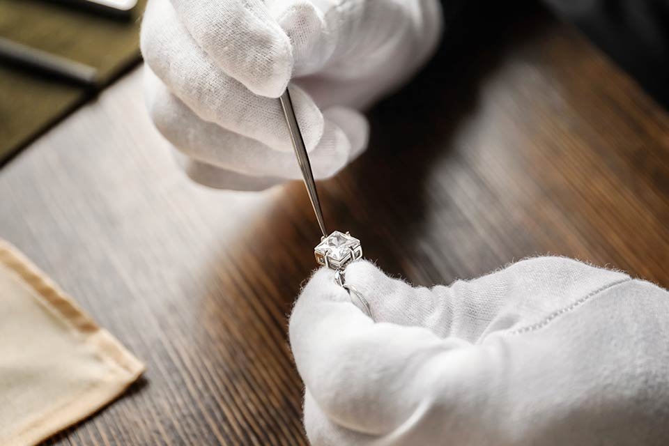 A person wearing gloves repairing a stone from a piece of jewellery.