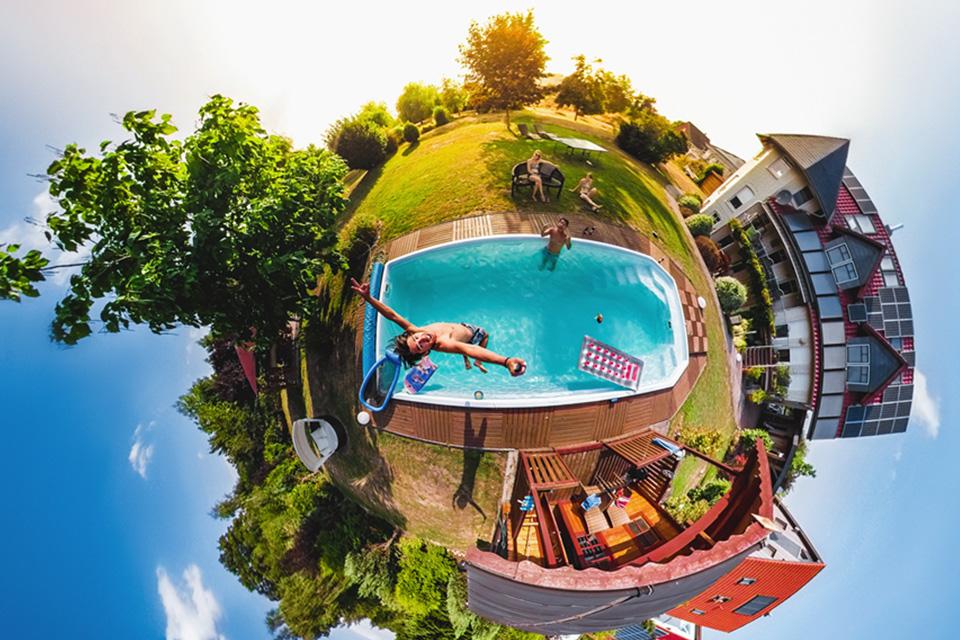 A boy jumps into a pool in a fish-eye lens shot which curves the world around him into a tiny planet.