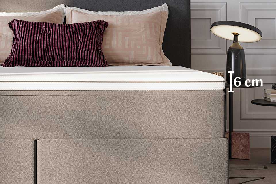 A close up of a mattress topper on a bed with pillows and a lamp in the back.