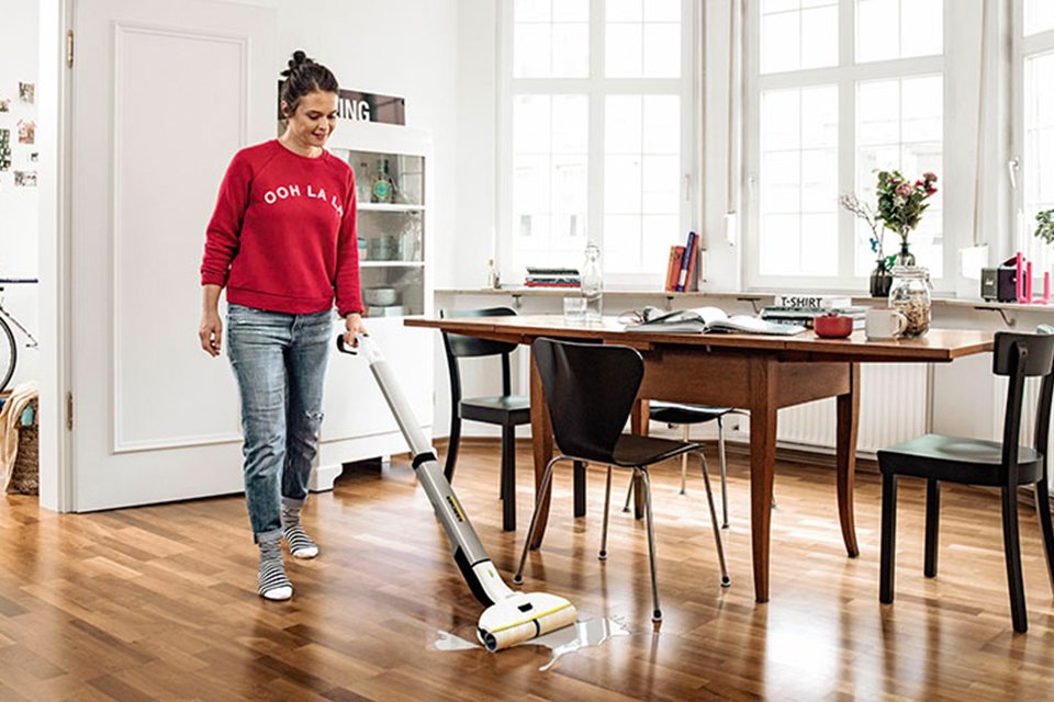 A woman using Kärcher hard floor cleaner machine on a wooden floor of her dining area.