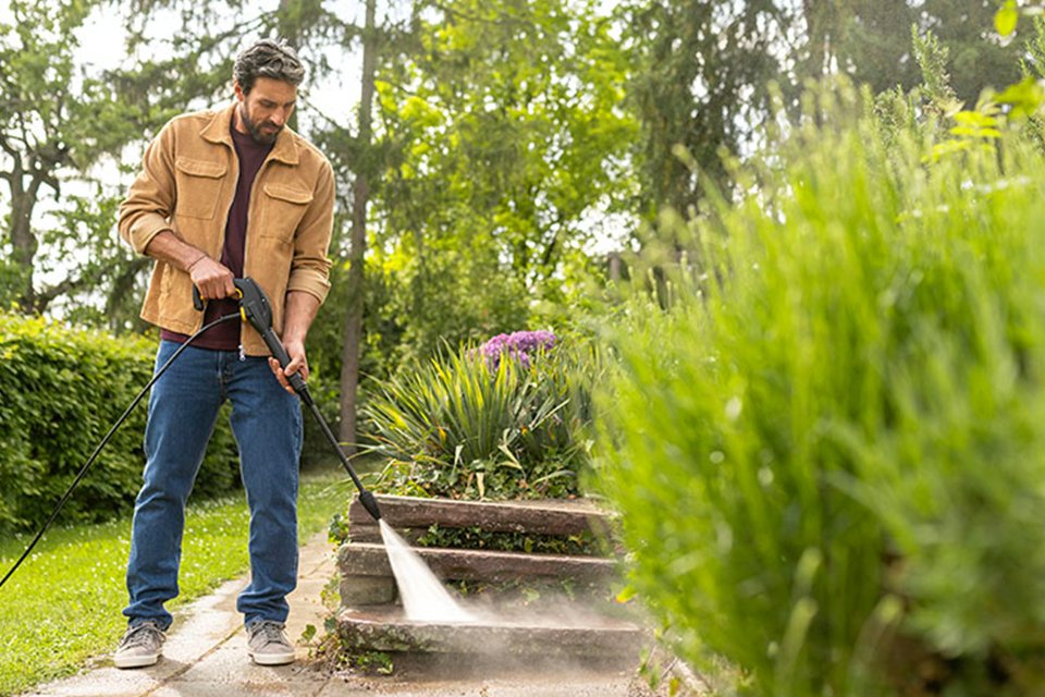 A man using Kärcher pressure washer against a garden pavement.