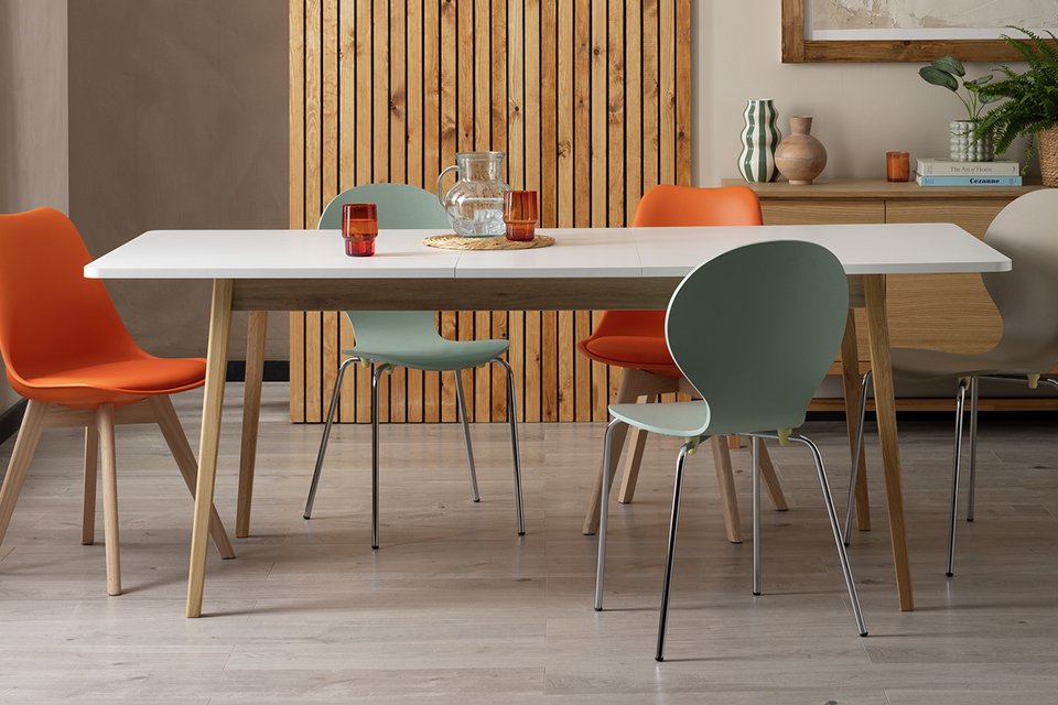 A Habitat Sylas Extending 6-8 Seater Dining white Table with orange chairs in a dining room.