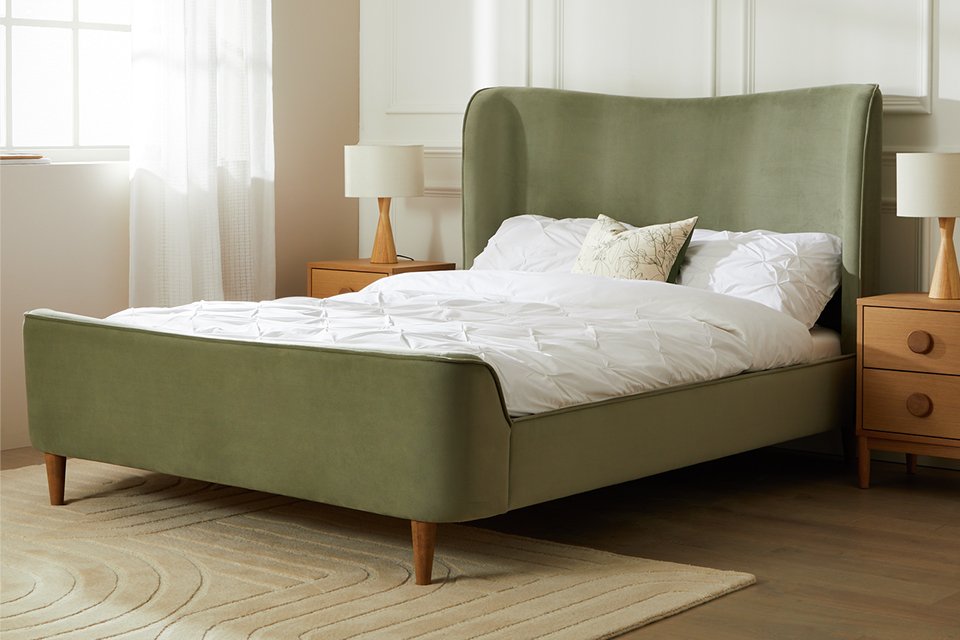 An olive green double bed with white bedding in a bedroom.