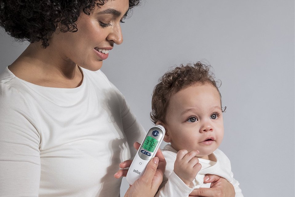 A mother checking her baby's temperature with Braun IRT6525 ThermoScan 7+ Ear Thermometer with Night mode.