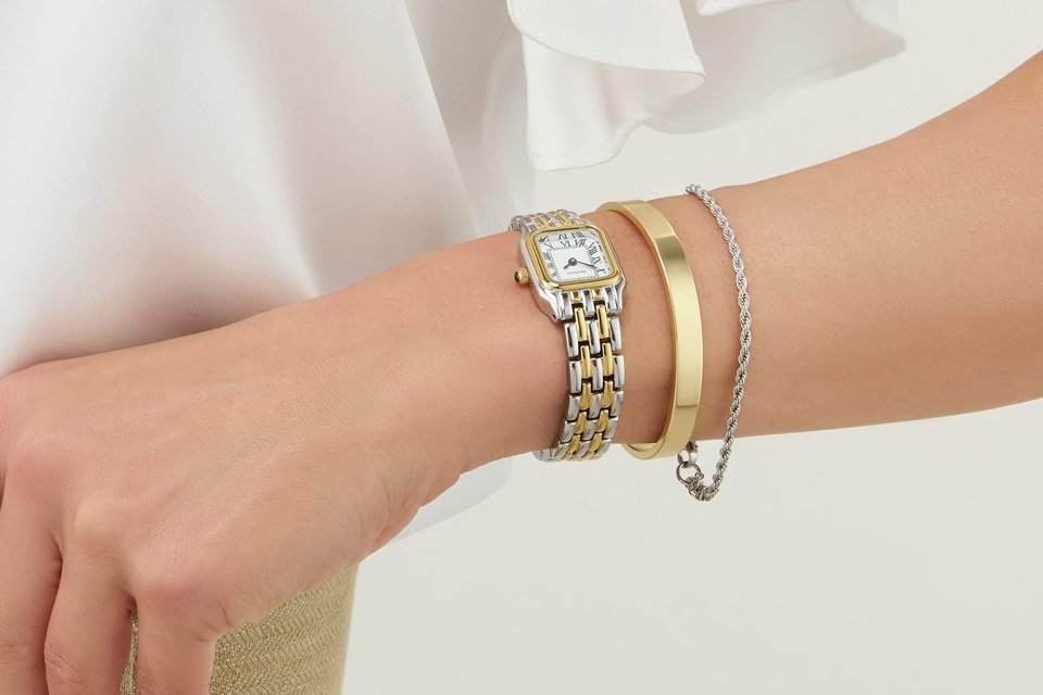 A woman wearing a watch and some gold bracelets on her arm.
