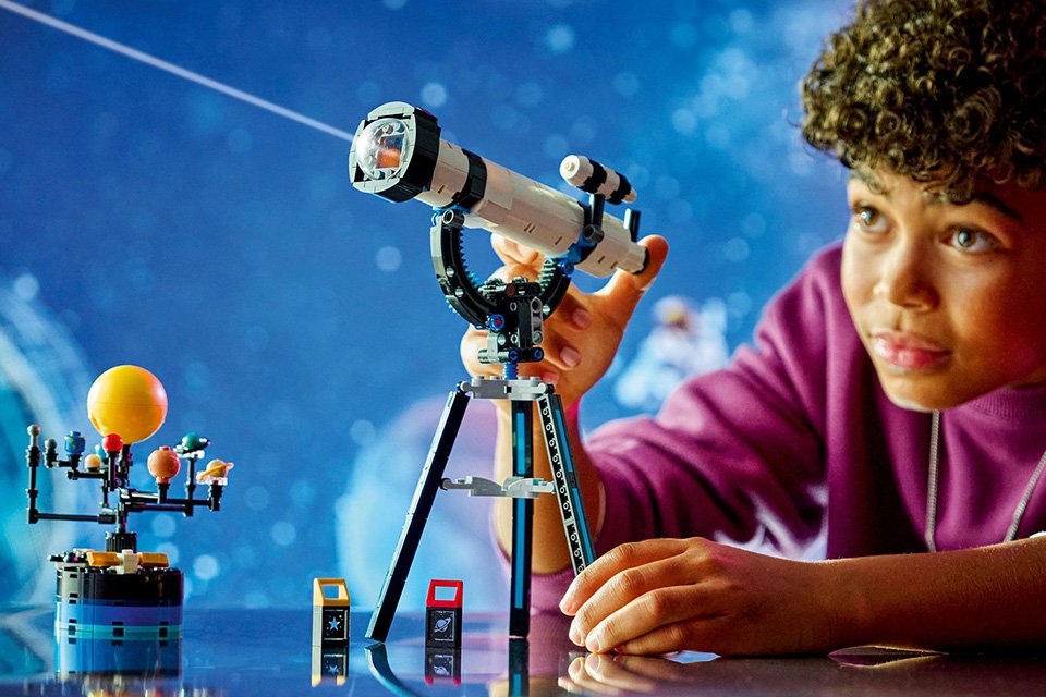 A boy playing with a LEGO Creator 3in1 space exploration telescope toy.