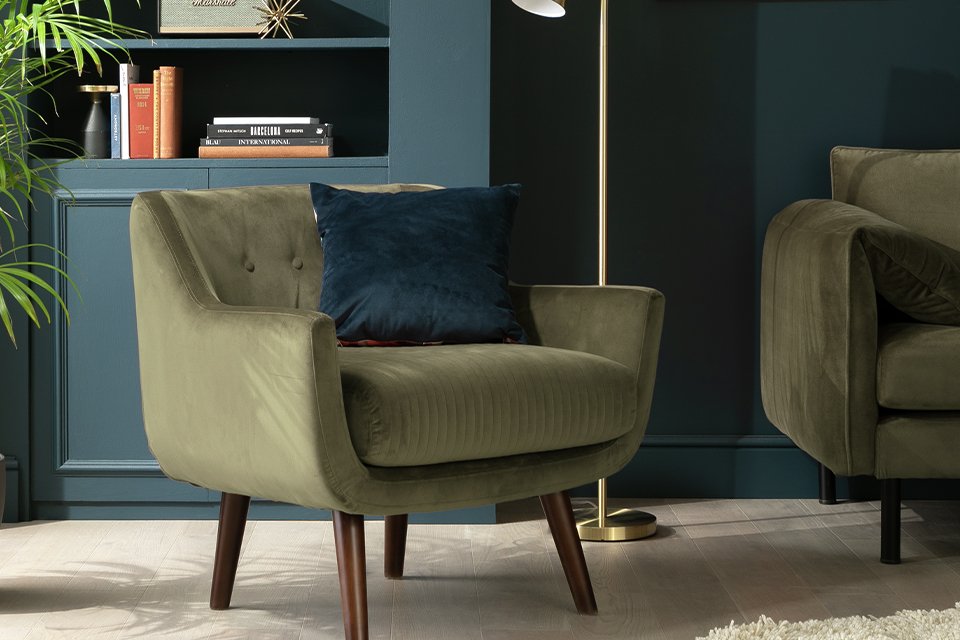A pillow, floor lamp and a cosy armchair near a bookshelf in a room.