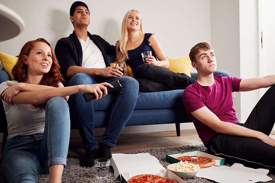 Group of students watching TV and eating pizza.