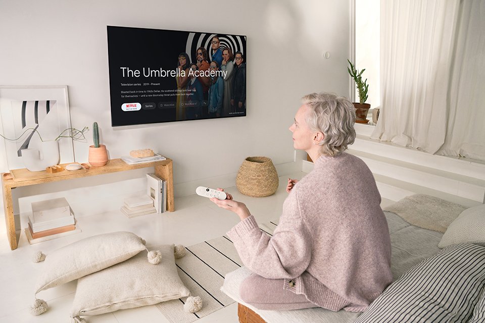 A woman sitting on a bed using Google Chromecast on a TV.