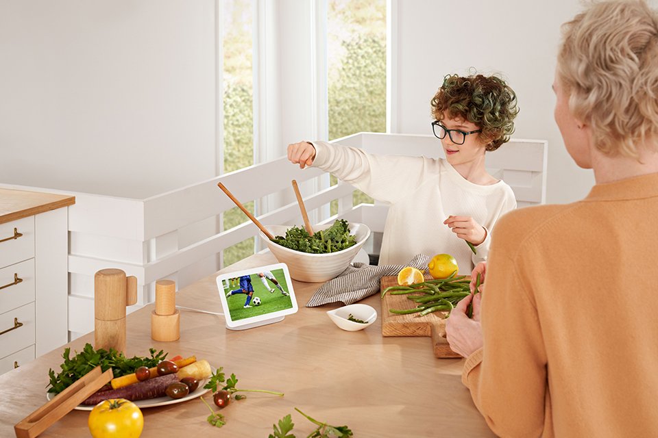 A woman and child watching a game on a Google Nest smart display placed on a dining table. 