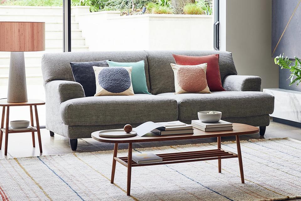 A grey made to order sofa with colourful scatter cushions in front of a long coffee table.